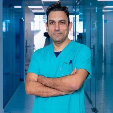 Dr Rafid Hussain in blue scrubs, arms folded, in a glass-walled clinic corridor.
