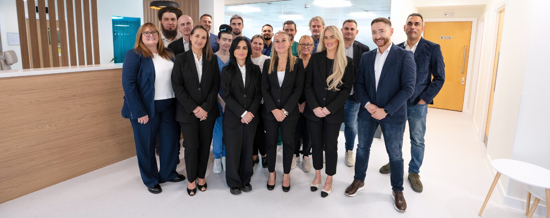 The Stockport Implant Centre team standing together in the clinic's reception, in front of the timber reception desk.